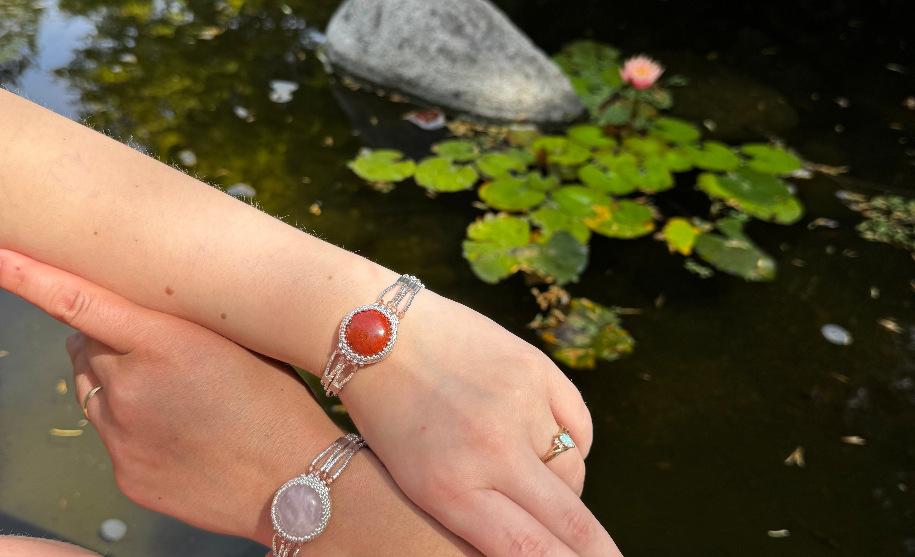 Two hands wearing silver bracelets with Red Jasper for Stability, courage, and strength in crystal healing; the other with Rose Quartz for compassion in crystal healing.